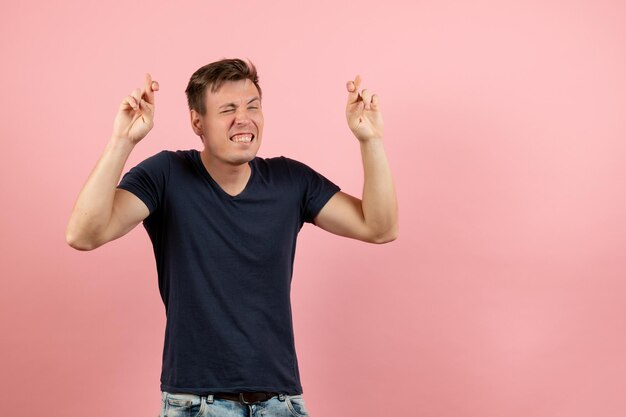 Vista frontal del hombre joven en camisa azul oscuro posando cruzando los dedos sobre fondo rosa