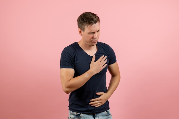 Foto gratuita vista frontal hombre joven en camisa azul oscuro que tiene problemas con el corazón sobre fondo rosa color humano hombre modelo emociones