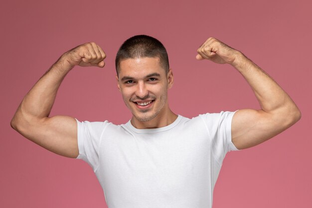 Vista frontal del hombre joven en camisa blanca flexionando con sonrisa sobre fondo rosa