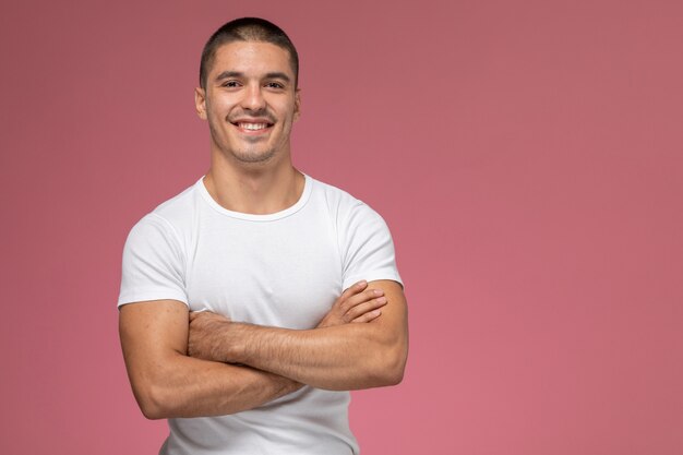 Vista frontal del hombre joven con camisa blanca mirando a la cámara y sonriendo sobre el fondo rosa