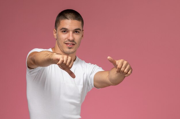 Vista frontal del hombre joven con camisa blanca posando con el dedo levantado sobre fondo rosa