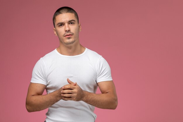 Vista frontal del hombre joven en camisa blanca posando en el escritorio rosa