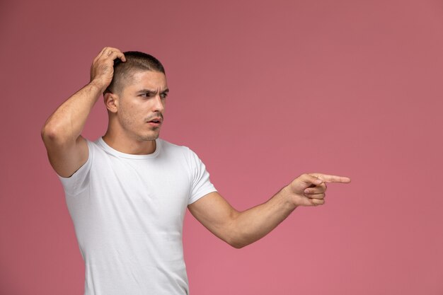 Vista frontal del hombre joven con camisa blanca posando con expresión confusa sobre el fondo rosa