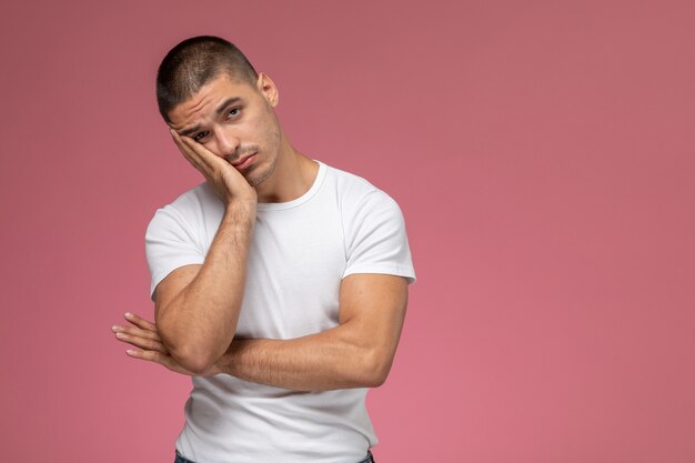 Vista frontal del hombre joven con camisa blanca posando con expresión estresada en el fondo rosa