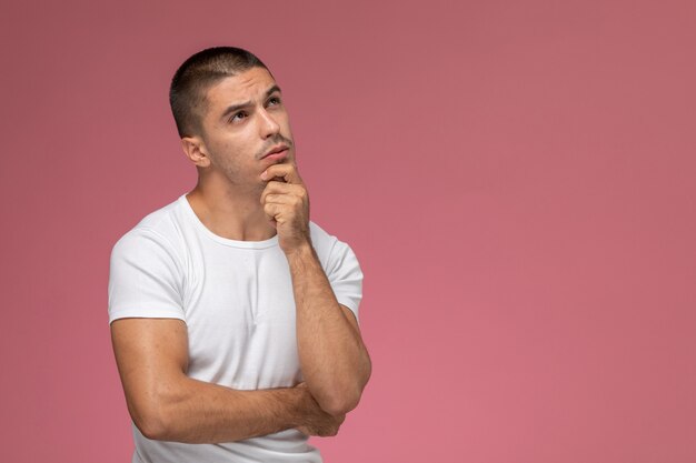 Vista frontal del hombre joven con camisa blanca posando con expresión de pensamiento sobre fondo rosa