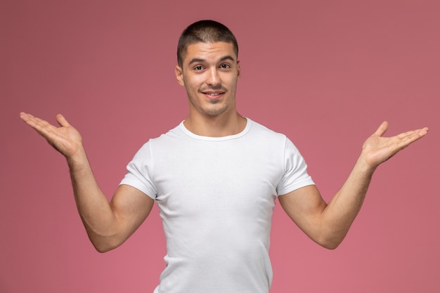 Vista frontal del hombre joven con camisa blanca posando con las manos levantadas sobre fondo rosa