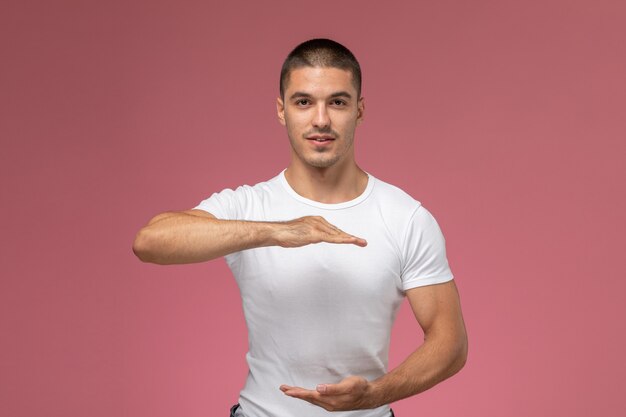 Vista frontal del hombre joven en camisa blanca posando con las manos sobre el fondo rosa