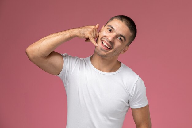 Vista frontal hombre joven con camisa blanca posando mostrando llamada telefónica sobre fondo rosa