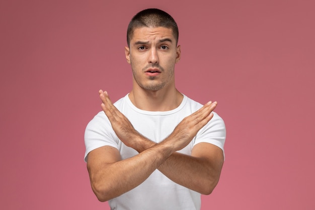 Vista frontal del hombre joven con camisa blanca que muestra el signo de prohibición sobre fondo de color rosa