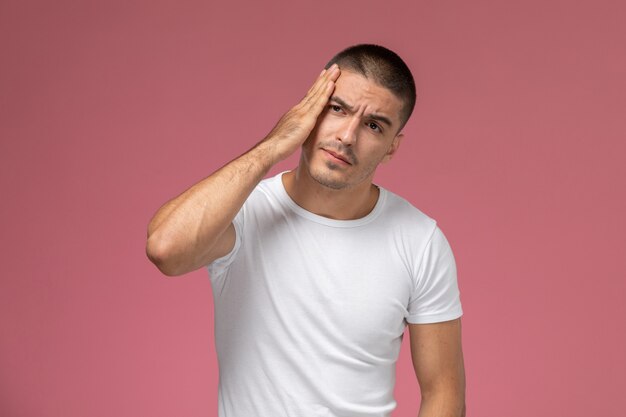 Vista frontal del hombre joven con camisa blanca sosteniendo su cabeza y rostro sobre fondo rosa