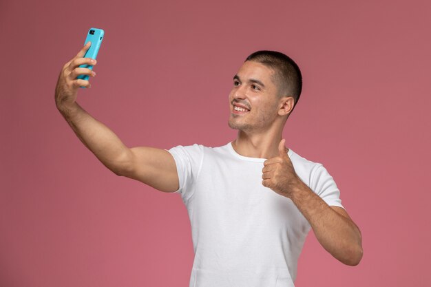 Vista frontal del hombre joven con camisa blanca tomando un selfie sobre fondo rosa
