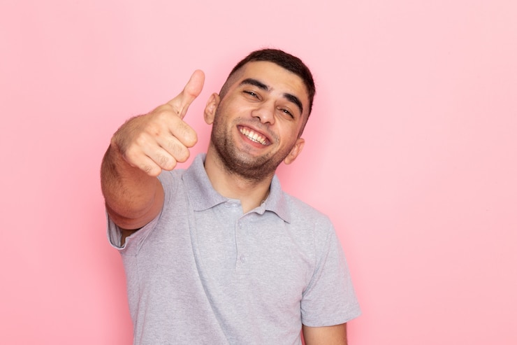 Foto gratuito vista frontal hombre joven en camisa gris posando y sonriendo mostrando signo impresionante en rosa