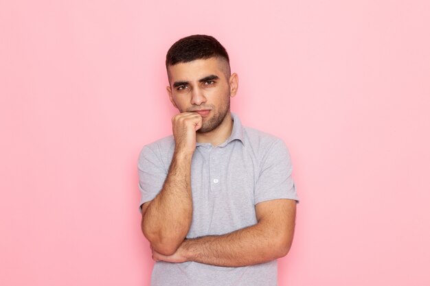 Vista frontal hombre joven en camisa gris posando con soporte de pensamiento en rosa