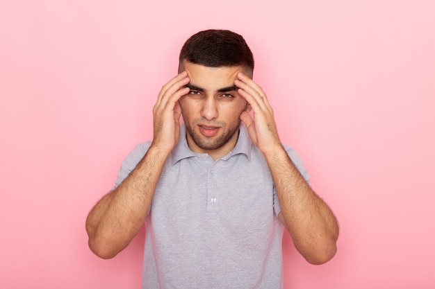 Vista frontal del hombre joven en camisa gris que tiene un dolor de cabeza severo en rosa