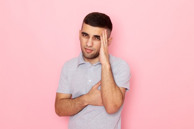 Vista frontal del hombre joven en camisa gris que tiene un fuerte dolor de cabeza en rosa