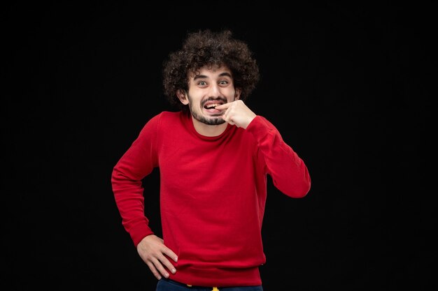 Vista frontal del hombre joven en camisa roja emocionado en la pared negra