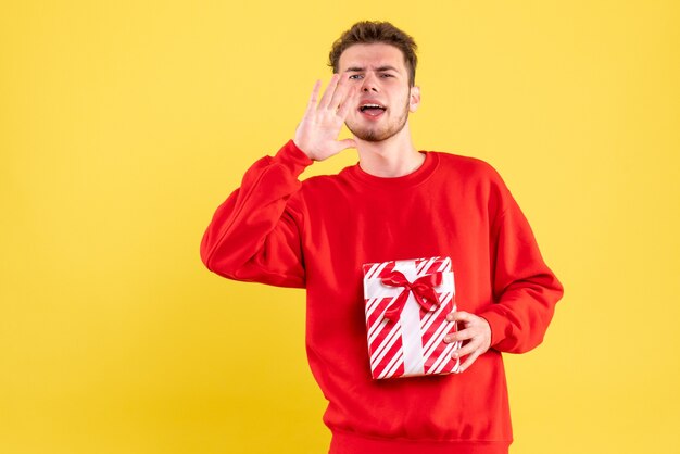 Vista frontal del hombre joven en camisa roja con regalo de Navidad llamando a alguien