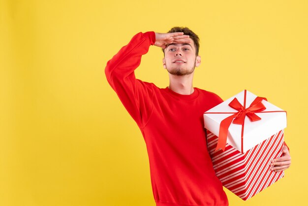 Vista frontal del hombre joven en camisa roja con regalo de Navidad mirando a distancia