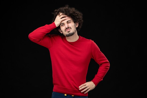 Vista frontal del hombre joven en camisa roja sobre pared negra