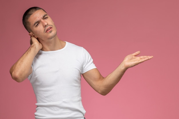 Vista frontal del hombre joven en camiseta blanca con dolor de cuello sobre fondo rosa