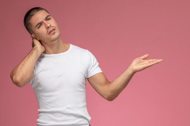 Vista frontal del hombre joven en camiseta blanca con dolor de cuello sobre fondo rosa