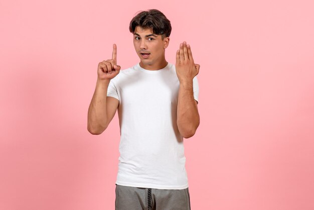 Vista frontal del hombre joven en camiseta blanca en el escritorio rosa