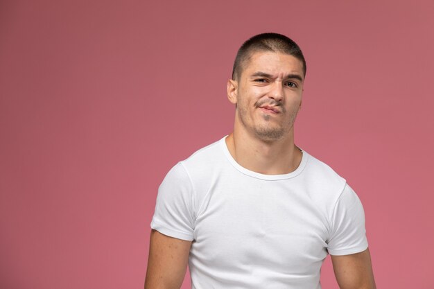 Vista frontal del hombre joven en camiseta blanca posando con expresión de disgusto sobre fondo rosa