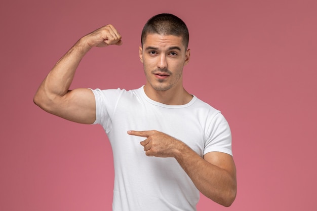Foto gratuita vista frontal del hombre joven en camiseta blanca posando flexionando sobre fondo rosa