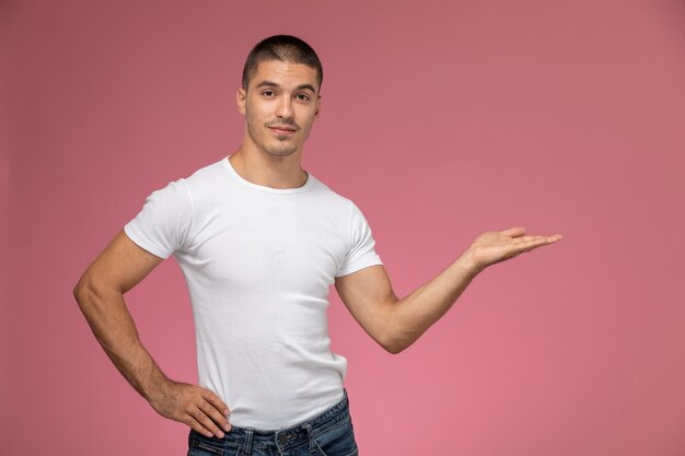 Vista frontal del hombre joven en camiseta blanca posando con la palma levantada sobre fondo rosa