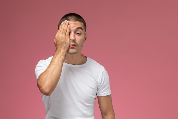 Vista frontal del hombre joven en camiseta blanca que cubre la mitad de su rostro sobre fondo rosa