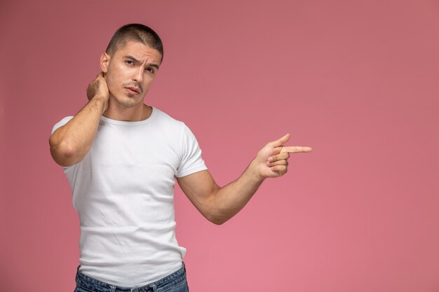 Vista frontal del hombre joven en camiseta blanca que sufre de dolor de cuello en el escritorio rosa