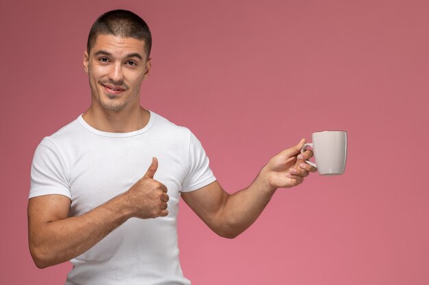 Vista frontal del hombre joven en camiseta blanca sosteniendo una taza de café en el fondo de color rosa