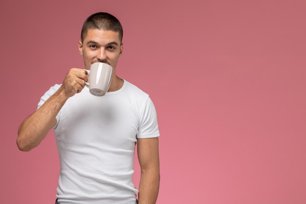 Foto gratuita vista frontal del hombre joven en camiseta blanca tomando café sobre fondo rosa
