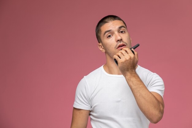 Vista frontal del hombre joven en camiseta blanca con walkie-talkie en escritorio rosa