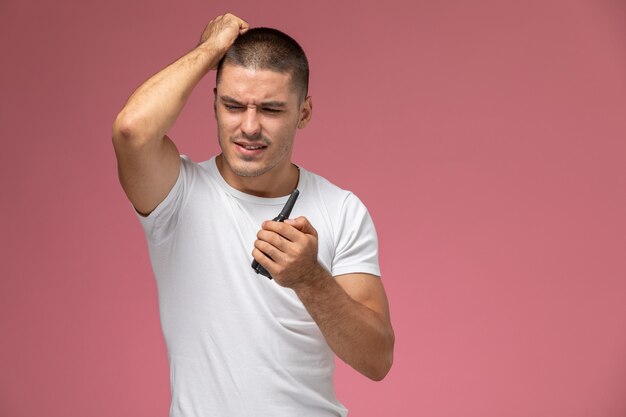 Vista frontal del hombre joven en camiseta blanca con walkie-talkie sobre fondo rosa