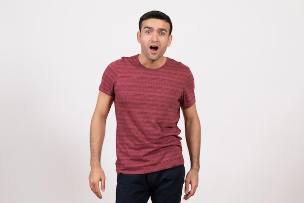 Vista frontal del hombre joven en camiseta de color rojo oscuro de pie con expresión de sorpresa sobre fondo blanco.