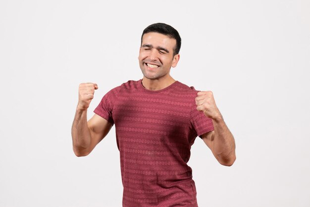 Vista frontal del hombre joven en camiseta de color rojo oscuro de pie y regocijándose sobre fondo blanco.