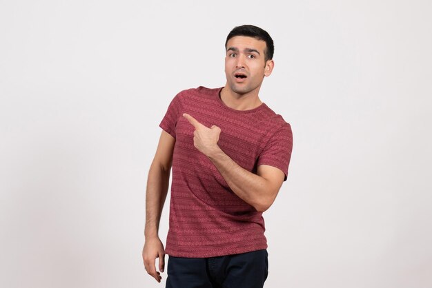 Vista frontal del hombre joven en camiseta de color rojo oscuro de pie sobre fondo blanco.