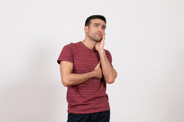 Vista frontal del hombre joven en camiseta de color rojo oscuro posando y pensando sobre fondo blanco.