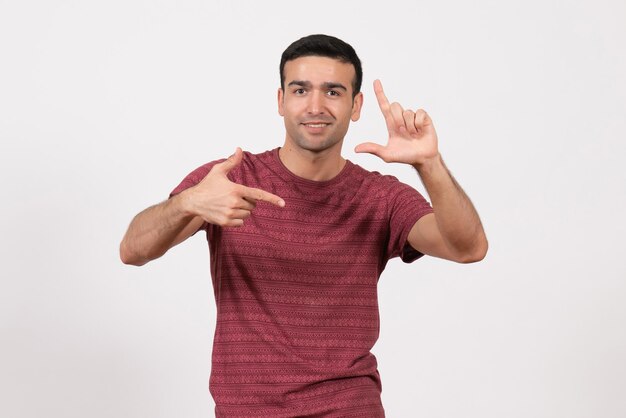 Vista frontal del hombre joven en camiseta de color rojo oscuro posando sobre fondo blanco claro