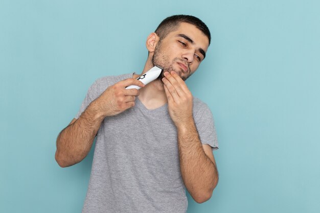 Vista frontal del hombre joven en camiseta gris afeitándose la barba en espuma de pelo masculino de barba de afeitado azul helado