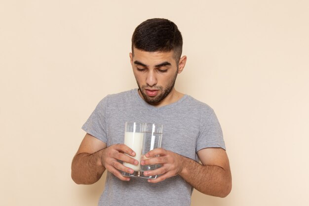 Vista frontal del hombre joven en camiseta gris y jeans con agua y leche en beige