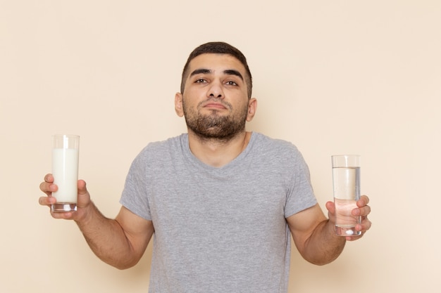 Vista frontal del hombre joven en camiseta gris y jeans con agua y leche en beige