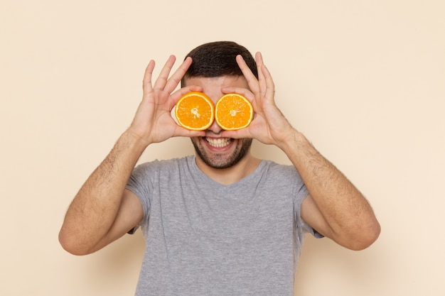 Foto gratuita vista frontal del hombre joven en camiseta gris y jeans azules sonriendo y sosteniendo anillos naranjas en beige