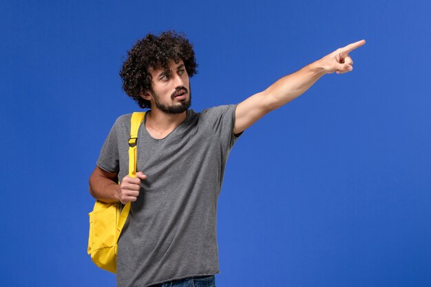 Foto gratuita vista frontal del hombre joven en camiseta gris con mochila amarilla en la pared azul