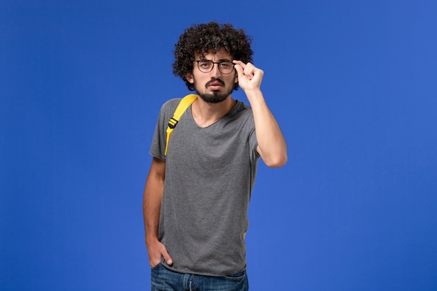 Vista frontal del hombre joven en camiseta gris con mochila amarilla en la pared azul