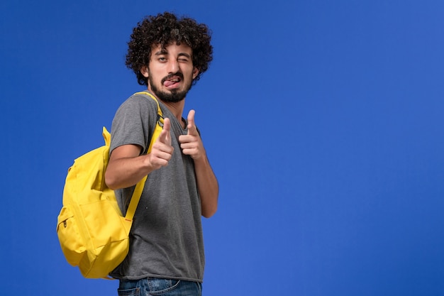 Foto gratuita vista frontal del hombre joven en camiseta gris con mochila amarilla en la pared azul