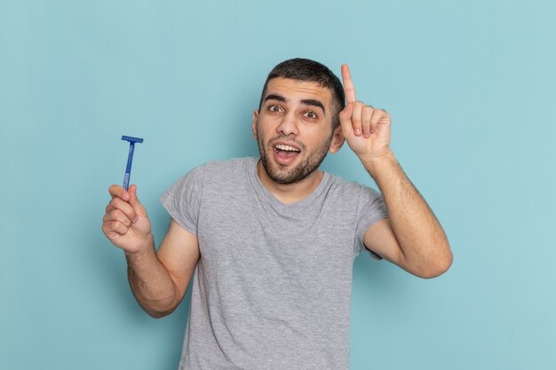 Vista frontal del hombre joven en camiseta gris con navaja en color azul de espuma de pelo de barba de afeitar