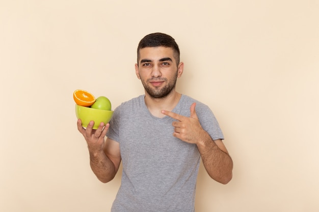 Vista frontal del hombre joven en camiseta gris con placa con frutas en beige