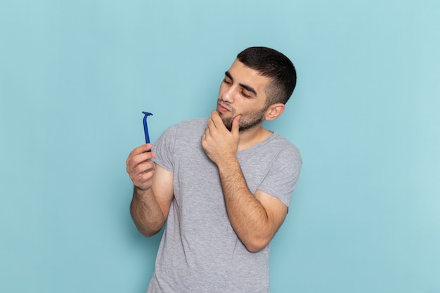 Foto gratuita vista frontal del hombre joven en camiseta gris sosteniendo la navaja y pensando en el azul